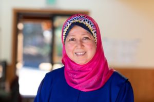 Huda Alkaff wearing a bright pink hijab and is smiling.