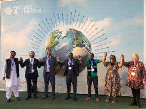 Group of Faith Leaders Holding Raided Hands in front of COP28 Image of a Globe