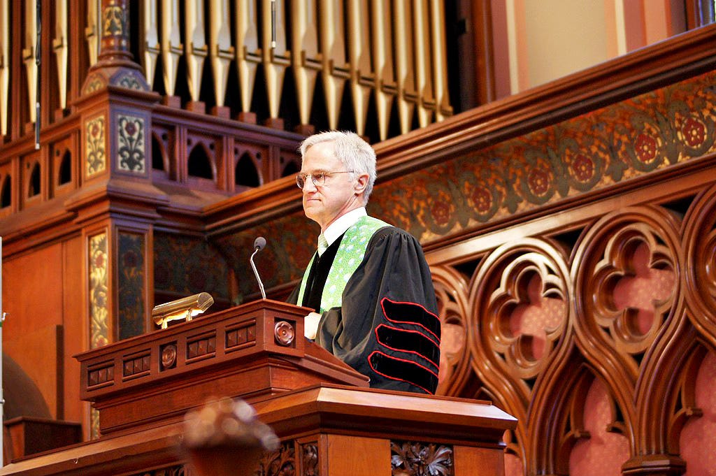 White Male with Gray Hair and Glasses Wearing Clergy Robe and Green Stole in Church Pulpit